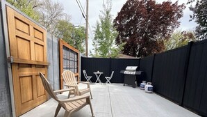 Een achtertuin met een barbecue, stoelen en een houten deur.