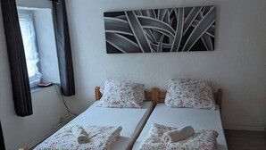 A room with two wooden beds, white bedding, a floral-patterned pillow, a wall-mounted abstract art piece, and a window with curtains. - 4 Persons apartment in the Eifel (Baustert)