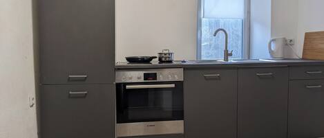 Une cuisine moderne avec des meubles gris, un four Bosch, un évier et une fenêtre donnant sur un beau paysage.