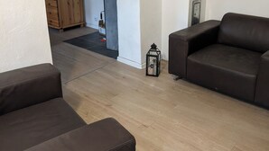 A modern living room with a brown leather sofa, a wooden wardrobe, and a small black lantern. - 4 Persons apartment in the Eifel (Baustert)
