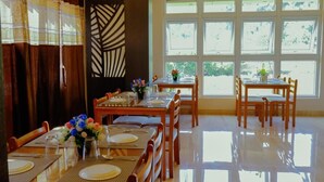 A dining area with tables set for four, large windows, and a decorative wall panel. - Andaman Beach Resort (Port Blair)