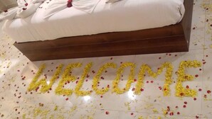 A bed with a white cover and a wooden headboard, surrounded by scattered rose petals on the floor. - Andaman Beach Resort (Port Blair)
