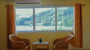 A room with two wicker chairs, a small table with a flower vase, and a window with curtains. - Andaman Beach Resort (Port Blair)