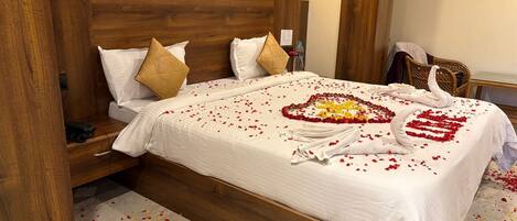 Een hotelkamer met een houten hoofdeinde, een bed met wit beddengoed en een decoratie in de vorm van een hart, gemaakt van rozenblaadjes.