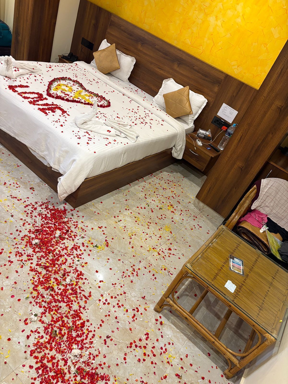 A hotel room with a bed, a wooden headboard, a nightstand, and a small table with a bottle and a remote control.