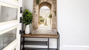 A framed picture of an archway with a view of a landscape, placed on a black metal stand against a white wall. - Modern 2 Bedroom Lakeview Suite (Kelowna)