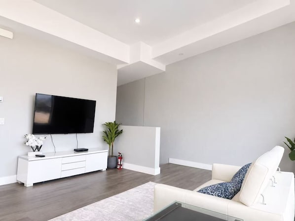 A modern living room with a flat-screen TV, white furniture, and a grey accent wall.