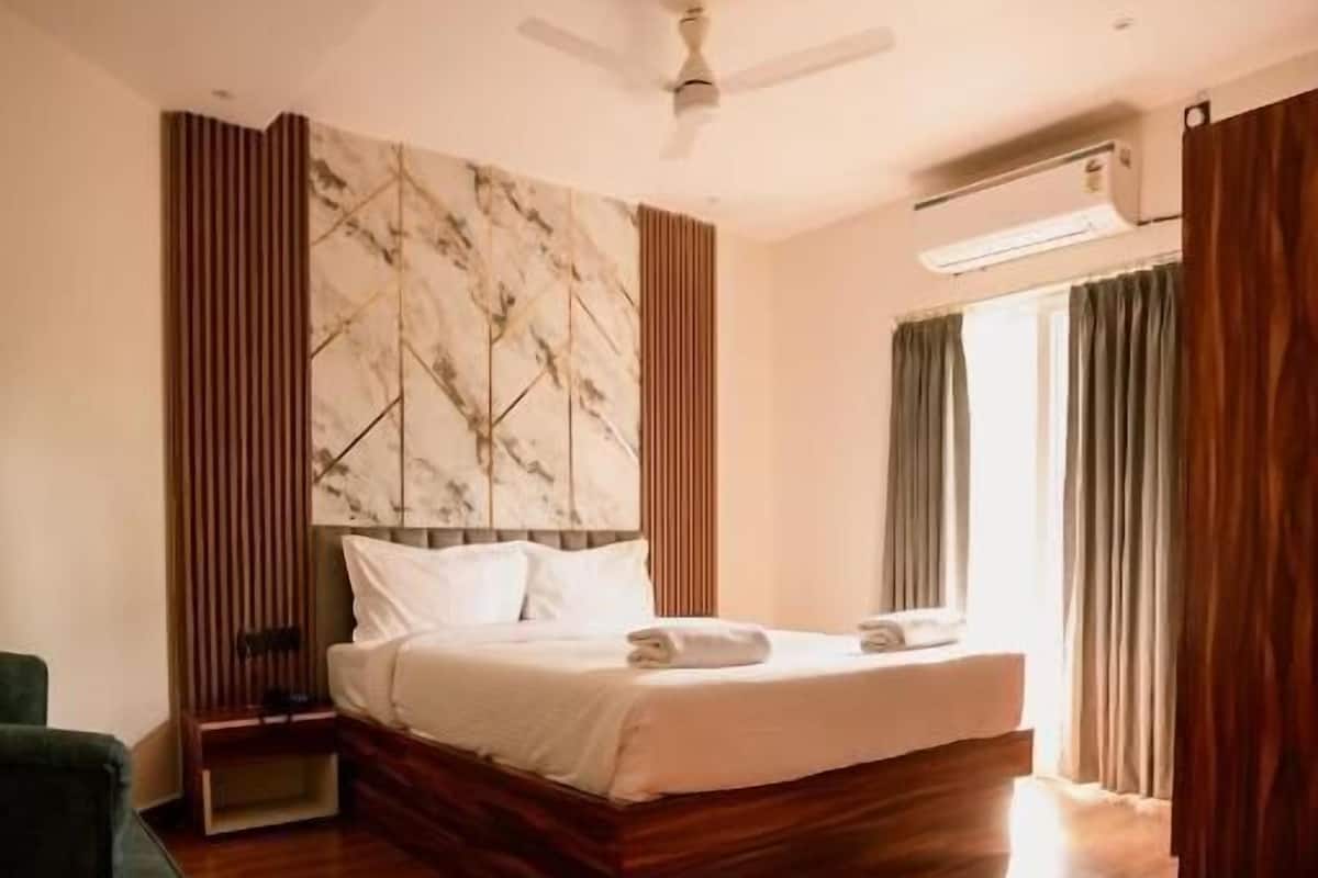 A bedroom with a bed, a ceiling fan, a nightstand, a green armchair, and a wooden floor.