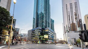 A modern urban intersection with tall buildings, including a prominent glass skyscraper and a cylindrical structure. - Exclusive Stays - SouthbankONE (Southbank)