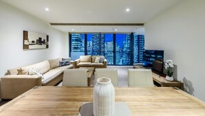 A modern living room with a large window, a sofa set, a coffee table, and a TV. - Exclusive Stays - SouthbankONE (Southbank)
