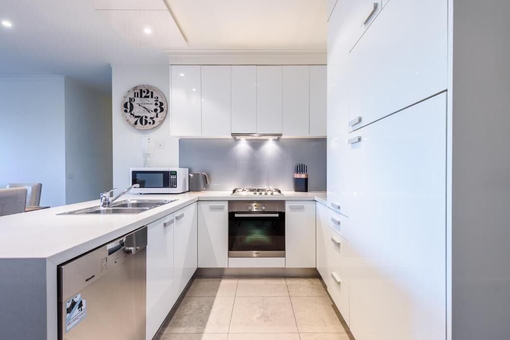 A modern kitchen with white cabinets, a built-in oven, a microwave, and a clock on the wall.
