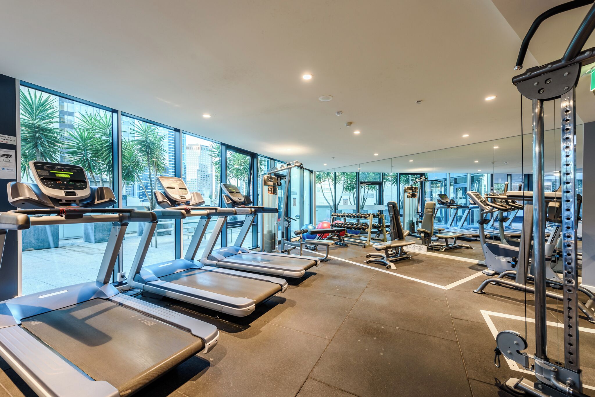 Een moderne sportschool met loopbanden, krachtapparaten en een groot raam met uitzicht over de stad.