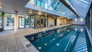An indoor swimming pool with a glass ceiling, adjacent to a modern building with large windows. - Exclusive Stays - SouthbankONE (Southbank)