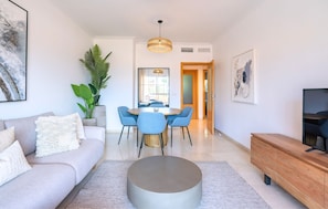 Ein modernes Wohnzimmer mit einer Couch, einem Couchtisch, einem Essbereich mit Stühlen, einem Fernseher und Kunstwerken an den Wänden.