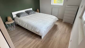 A bedroom with a bed, a window, a radiator, and a wooden floor.