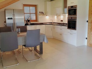 Une cuisine moderne avec des armoires blanches, des appareils en acier inoxydable et un coin repas comprenant une table et des chaises.