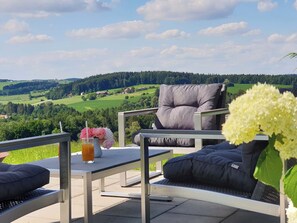 Eine Terrasse mit Tisch, Stuhl und Blick auf eine grüne Landschaft.