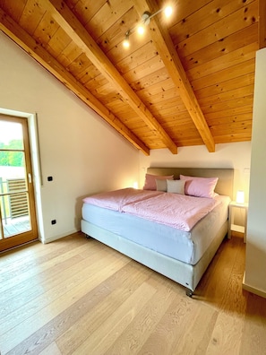 Une chambre avec un plafond en bois, un lit avec une literie rose et une table de chevet avec une lampe.