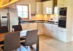 Eine moderne Küche mit weißen Schränken, einem eingebauten Ofen und einem Essbereich mit einem Holztisch und Stühlen.