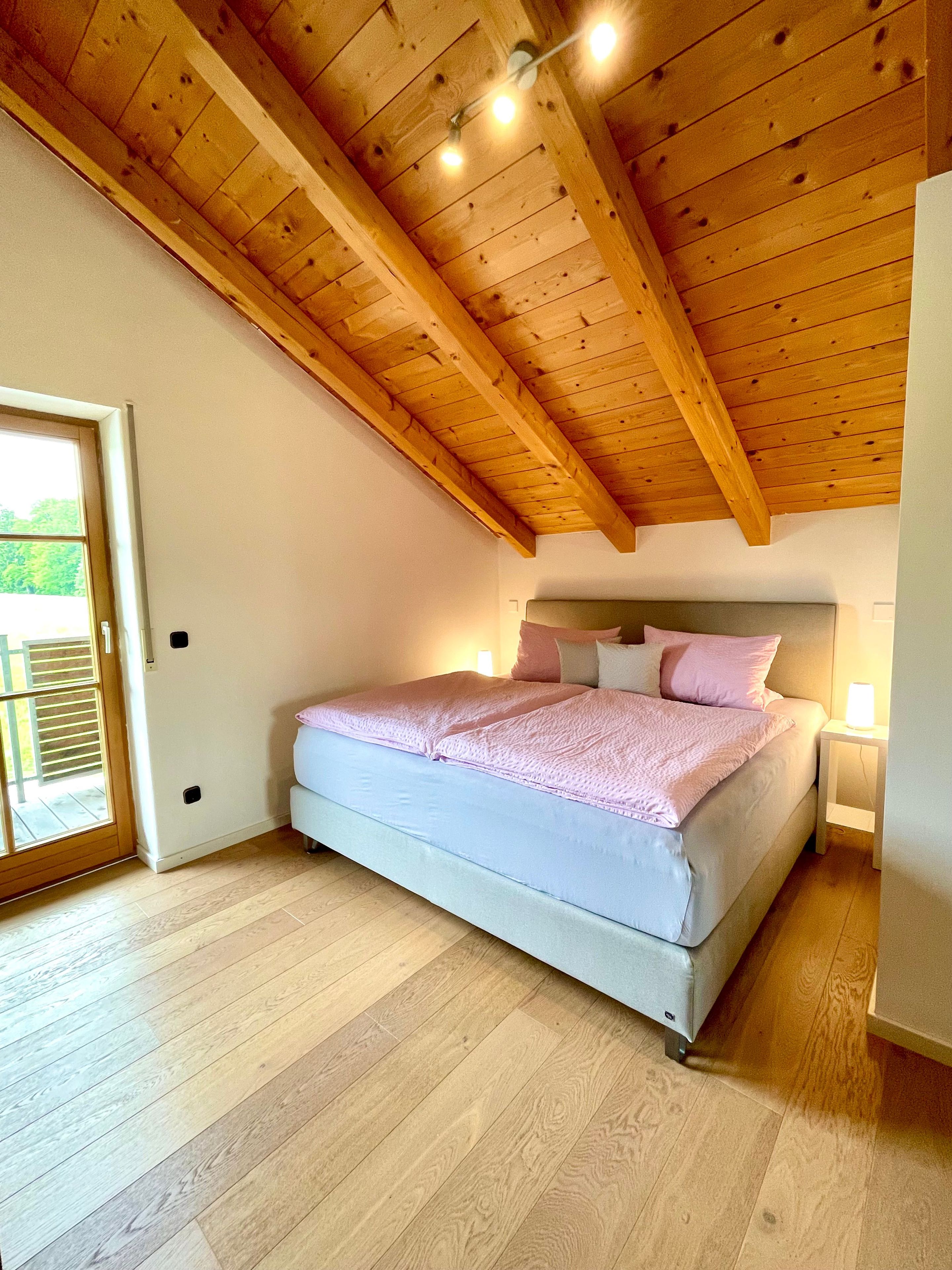Una camera da letto con soffitto in legno, un letto con testiera, un comodino e una finestra.