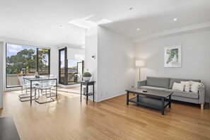 A modern living room with a grey sofa, a coffee table, and a dining area with a glass table and chairs. - Spacious 1 Bed Apartment Near St Kilda Beach (St Kilda)