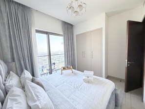 Ein Schlafzimmer mit einem großen Bett, Blick auf die Stadt, einem Kleiderschrank und einer Tür.