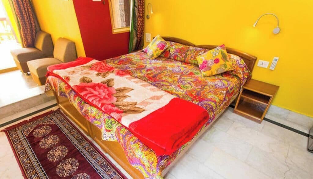 Ein Bett mit farbenfroher Bettdecke, einer roten Decke und einem gemusterten Teppich.