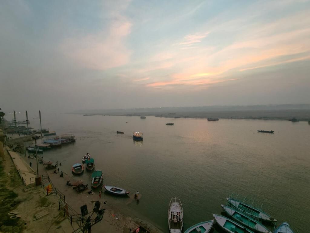 A river with boats docked along the shore, a distant city skyline, and a clear sky.