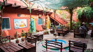 An outdoor patio with wooden benches, a fountain, and potted plants. - Ganpati Guest House (Varanasi)
