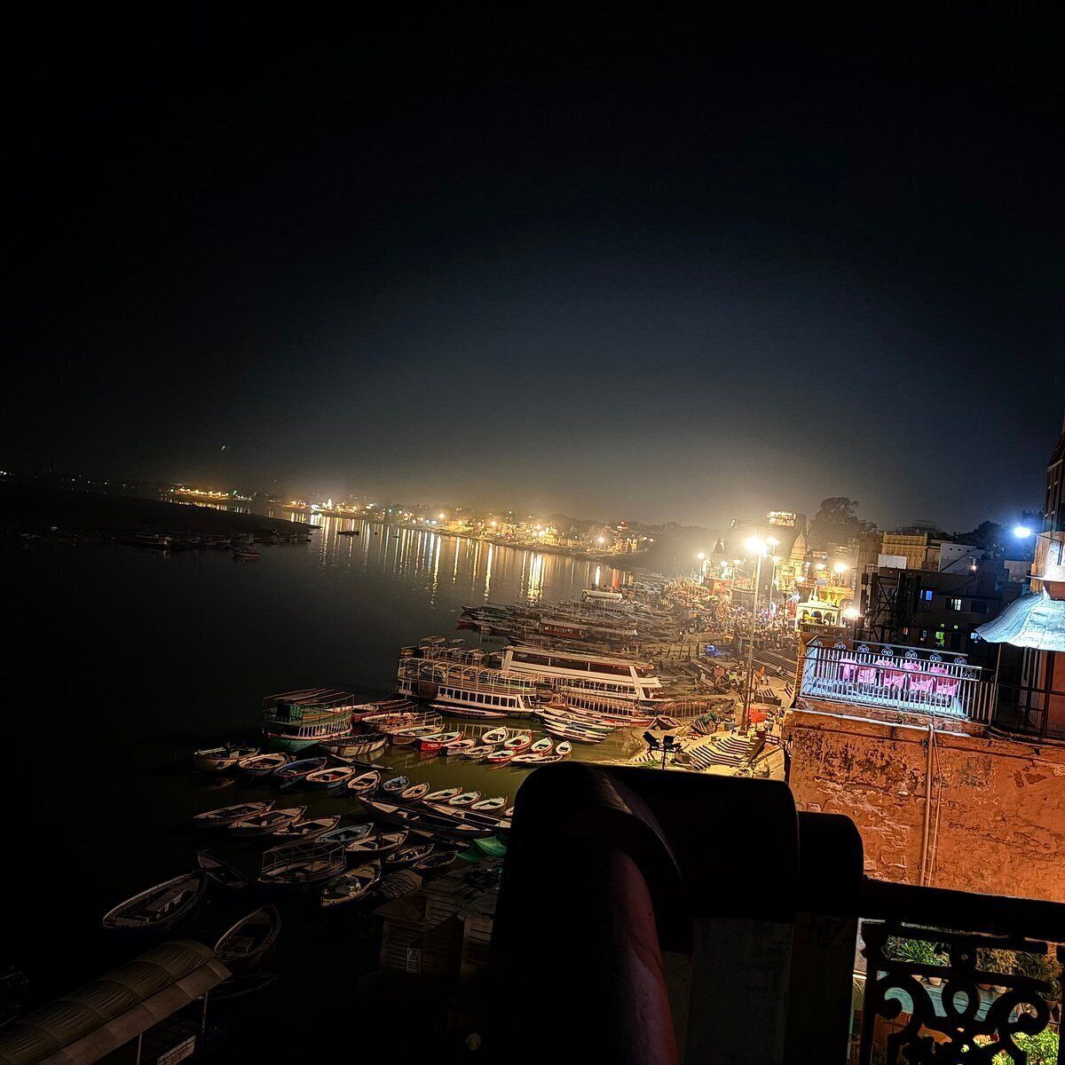 A nighttime view of a riverside area with boats docked along the shore and buildings illuminated in the background.
