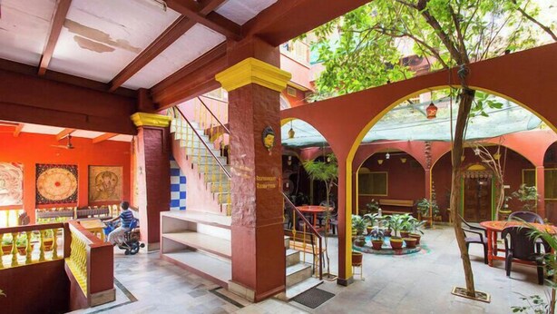 A multi-level atrium with a staircase, columns, and potted plants. - Ganpati Guest House (Varanasi)