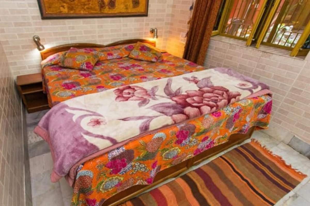 Una habitación con dos camas, una colcha estampada, un cabecero de madera, una mesita de noche, un cuadro colgado en la pared y una ventana con vistas.