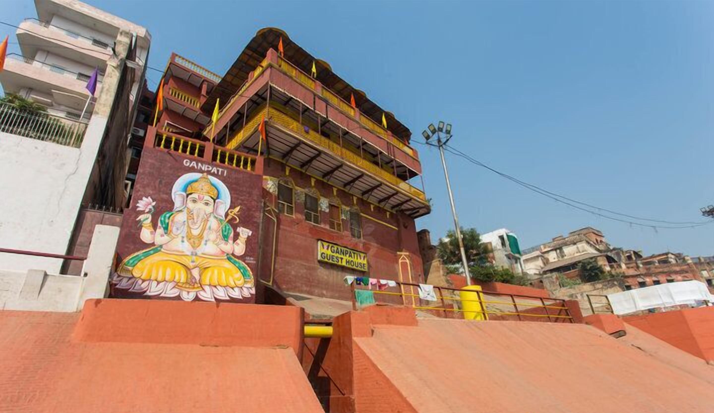 A building with a mural of a deity, a sign indicating a guest house, and a multi-story structure with balconies.