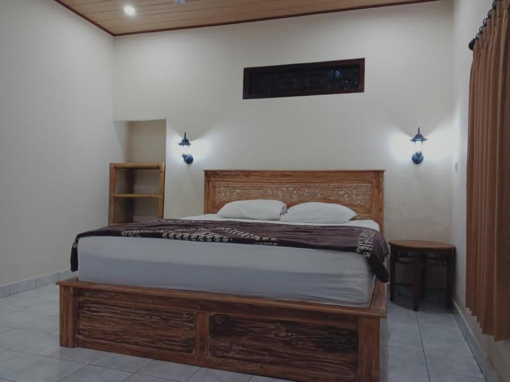 A bedroom with a wooden bed, two wall-mounted lights, a small wooden nightstand, and a shelf unit.