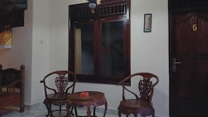 A room with two wooden chairs, a small round table, a large window with a dark wooden frame, and a door with the number 5. - Sudana Homestay Ubud (Ubud)