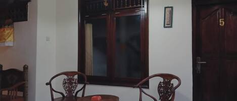 Une pièce comprenant deux chaises en bois, une petite table ronde, une grande fenêtre avec un cadre en bois foncé et une porte portant le numéro 5.
