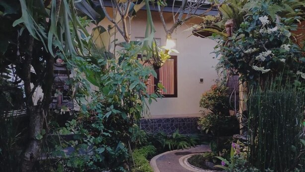 A garden pathway leading to a building with a window and a hanging light fixture. - Sudana Homestay Ubud (Ubud)
