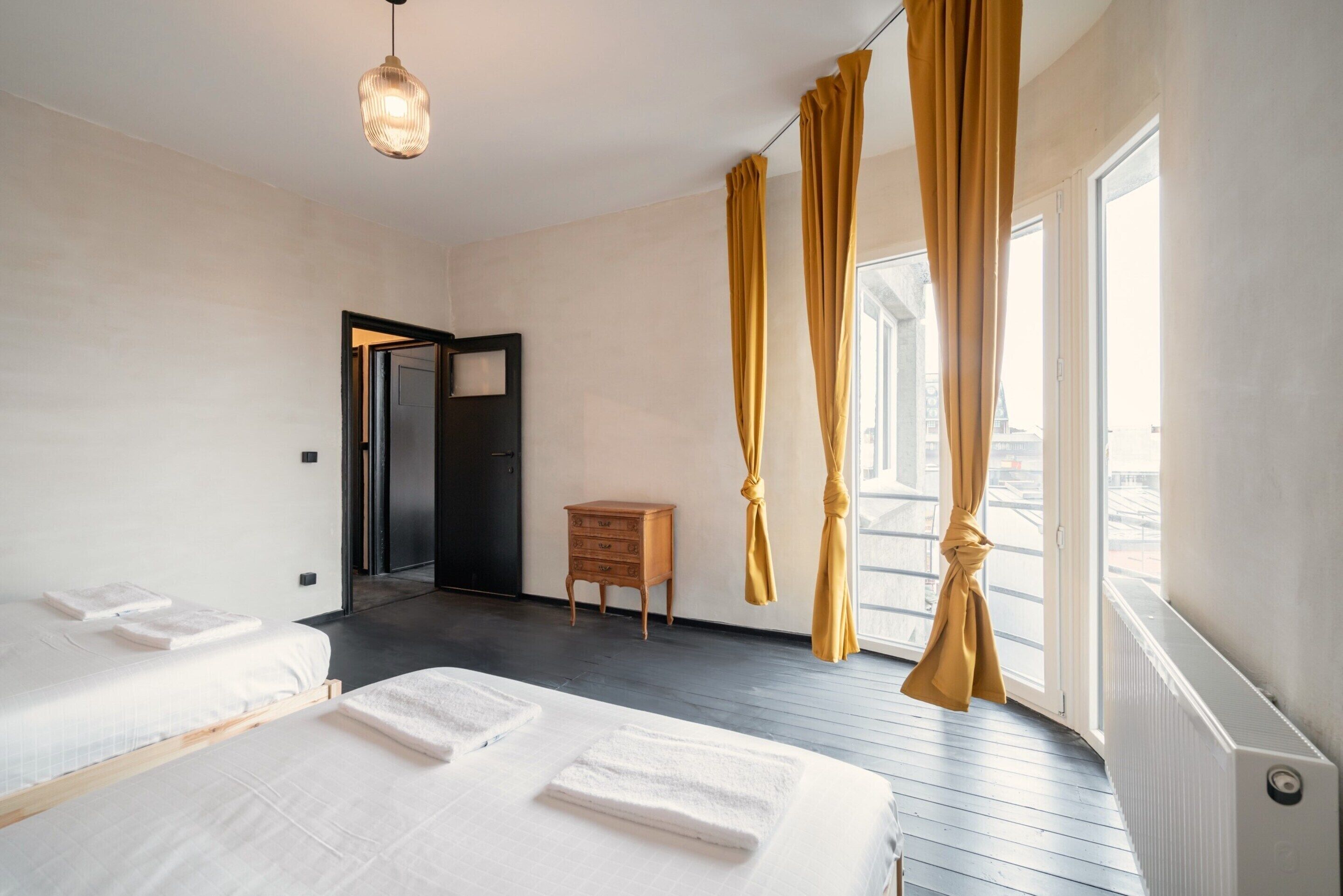 Een hotelkamer met twee bedden, een houten nachtkastje, een deur en een raam met gordijnen.