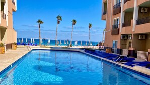 Ein Pool mit Liegestühlen, Palmen und Blick aufs Meer.