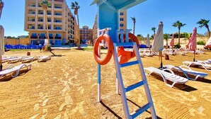 Ein Strand mit Liegestühlen, einem Rettungsschwimmerstand und einem Gebäude im Hintergrund.