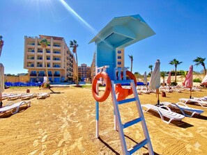 A beach with sun loungers, a lifeguard stand, and a building in the background. - Romantic apartment with garden, pool and beach (Hurghada 2)