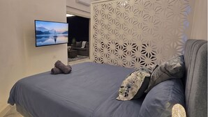 Ein Schlafzimmer mit Bett, Kissen, Fernseher und einem dekorativen Raumteiler.