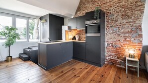 A modern kitchen with dark cabinetry, a brick wall, and a wooden floor. - Two-bedroom Apartment by the River (Antwerp)