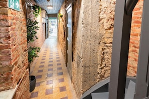 A narrow corridor with brick walls, a checkered floor, and a door on the right.