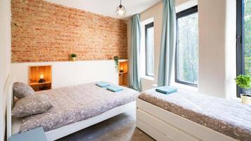 Una habitación con dos camas, una pared de ladrillo, una ventana con cortinas y una lámpara colgante.