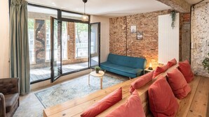A modern living room with a blue sofa, wooden bench with red cushions, a small table with a plant, and a brick wall. - The Industrial Apartments 2bbknsinternet (Antwerp)