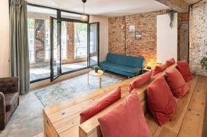 Una sala de estar moderna con un sofá azul, un banco de madera con cojines rojos, una mesita con una planta y una pared de ladrillo.