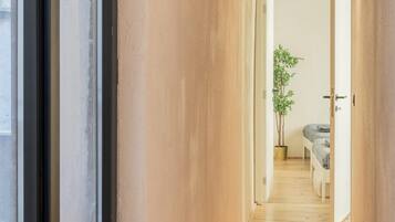 A narrow hallway with wooden flooring, a potted plant, and a bed in the distance.