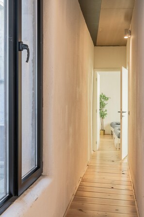 Un pasillo estrecho con suelo de madera, una planta en maceta y una cama al fondo.