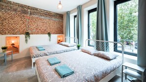 A room with two beds, a brick wall, a window, and a hanging plant. - The Industrial Apartments 2bbknsinternet (Antwerp)